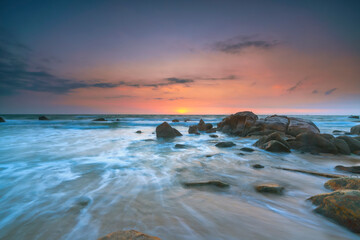 Obraz premium Beautiful coastal sunrise scene featuring a dramatic rock formation rising from a sandy beach.
