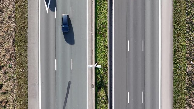 divided highway three cars traveling opposite directions separated by narrow green median shadows clearly marked lanes area long top down aerial view belgium 