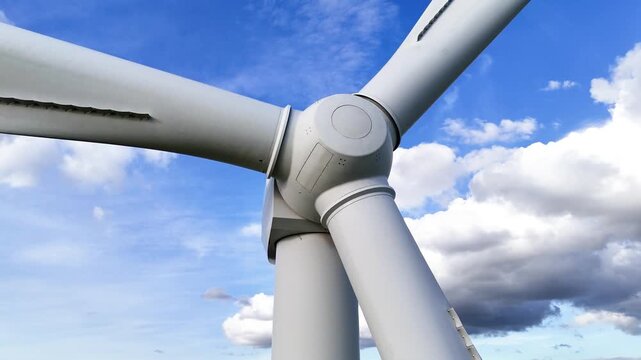 wind turbine central hub three blades framed by bright blue sky scattered cumulus clouds white surfaces sturdy up close smooth upward view close-up sweeping 