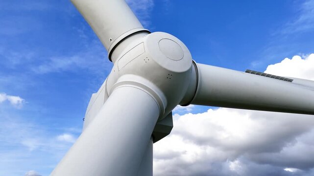 below wind turbine rounded hub thick white blades converging center against vivid blue sky drifting clouds accentuating structure scale from up close dramatic close-up clean design 