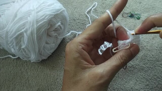Close up of hands crocheting yarn with a hook, creating textured stitches in a relaxing handmade craft process. The scene highlights traditional crochet technique, soft yarn movement.