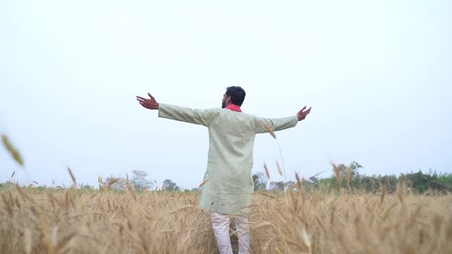 Young indian farmer standing at wheat agriculture field	