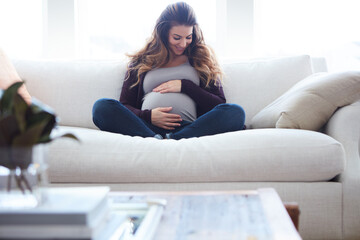 Obraz premium Smile, pregnant woman and touch stomach on sofa for motherhood, maternity and affection. Happy, female person and abdomen for fetal movement, prenatal connection and bonding with unborn baby at house