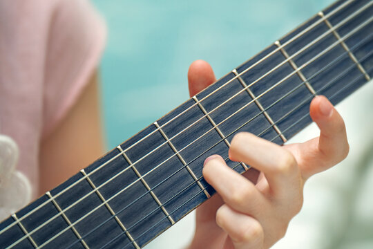 Teenage girl's hand pressing chords on a six-string guitar fretboard. Music learning and practice moment.