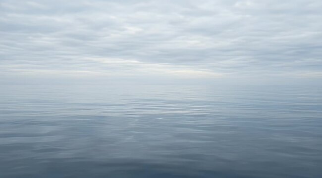Expansive tranquil sea beneath a soft grey cloudy sky, gentle waves reflect light