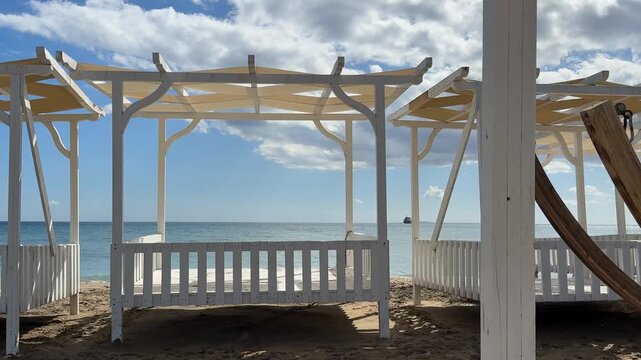 Beach cabanas with wooden frames on sandy shore under bright sky, suitable for background use