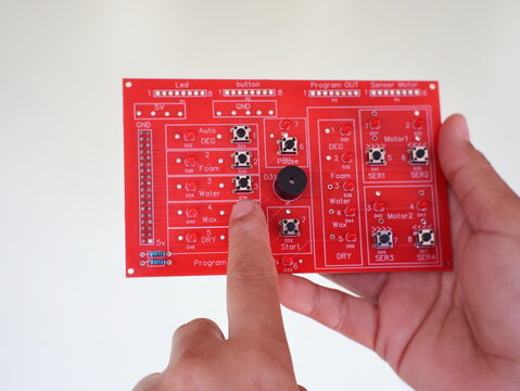 A finger points to a red electronic control circuit board for an automatic car wash system project.