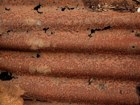 A close-up shot of heavily rusted and corroded corrugated iron, featuring deep orange oxidation and various holes caused by long-term weathering.