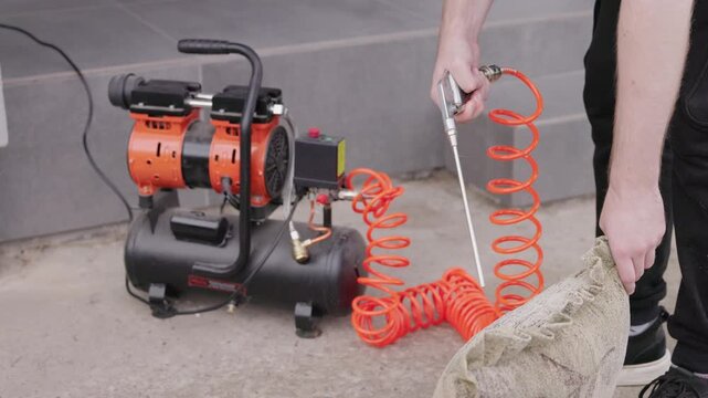 Cleaning pillow with compressed air using air compressor, blowing dust from cushion outdoors during home cleaning