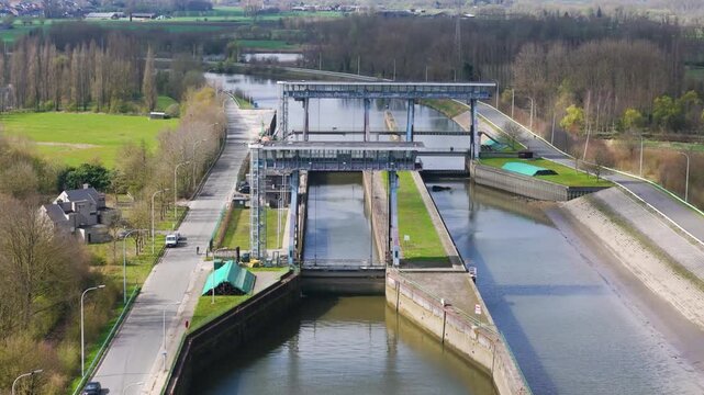twin lock chambers bordered by two massive steel lift gates glass control bridges reflect calm water tree lined roads grassy embankments farmland stretch into muted countryside reflection 