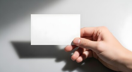 Fototapeta premium Hand holding blank white business card, shadow on gray background, professional template for branding and marketing