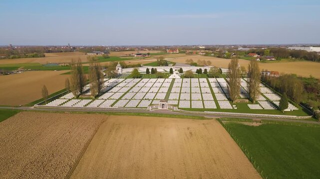 tyne cot cemetery gleaming headstones form immaculate grids central cross sacrifice curved memorial wall slender poplar trees border site surrounded by golden ploughed fields toward 