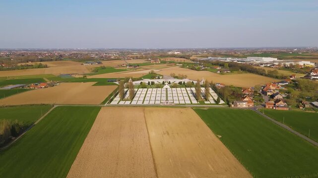 tyne cot cemetery forms luminous grid white headstones centered rolling agricultural plains nearby red roofed houses distant industrial buildings dot horizon under cloudless broad wwi 
