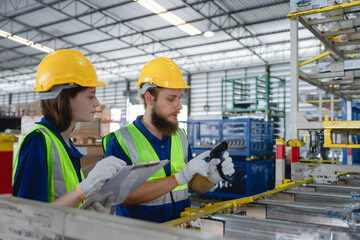 Industrial warehouse environment with Caucasian logistics workers wearing safety helmets and reflective vests while checking inventory data using handheld barcode scanner, warehouse management concept © AU USAnakul