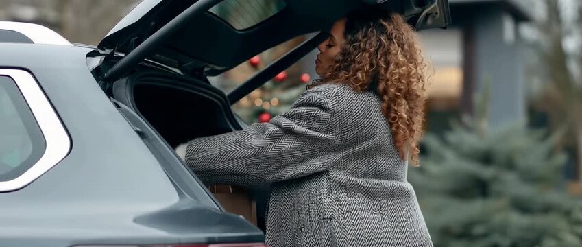 A lady is seen from the side loading her luggage into a car's trunk after shopping.