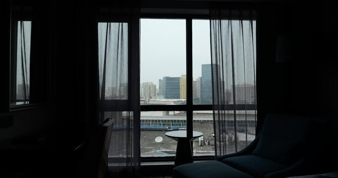 Two layers of curtains, sheer semi-transparent and blackout, closing one after another automatically. translucent layer begins to slide first, followed by blackout, obscuring overcast urban view