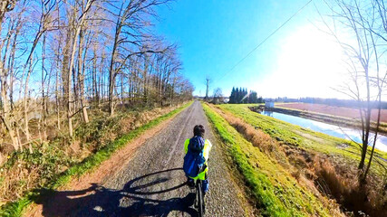 First-person view of a cyclist in a yellow jacket riding through scenic rural farmland with mountains on a sunny day in British Columbia. © Jeff
