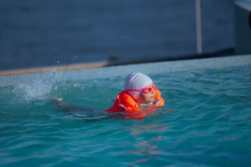 Child Swimming in Pool Wearing Protective Equipment. Happy child having fun during summertime vacation at fun resort
