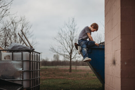 Young boy sitting on shop dumpster edge