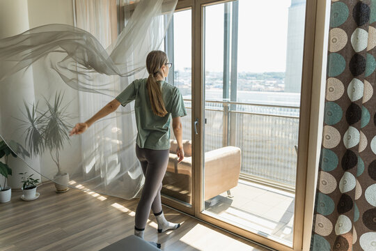 Woman approaches sunlit balcony with flowing curtains