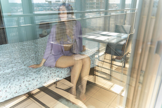 Woman sitting on bed reflected in glass door, abstract composition