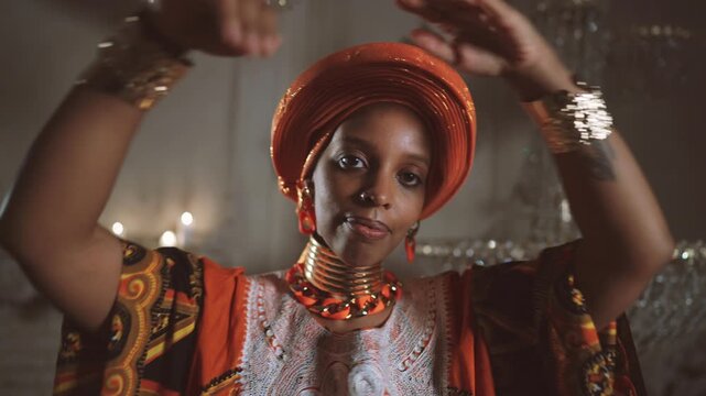 Unique dance show, beautiful black woman in traditional gown and turban dancing. African lady looking at camera and showing her gold bracelets on graceful wrists, rich and luxury jewelry for women