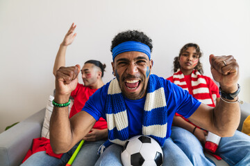 Fototapeta premium Group of excited multiethnic friends watching soccer match at home, screaming and celebrating a goal
