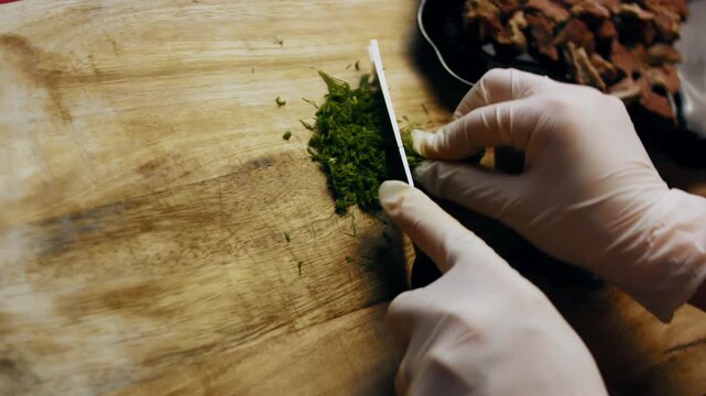 Fresh dill being finely chopped on a wooden surface