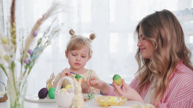 Happy mother and child decorating Easter eggs at home