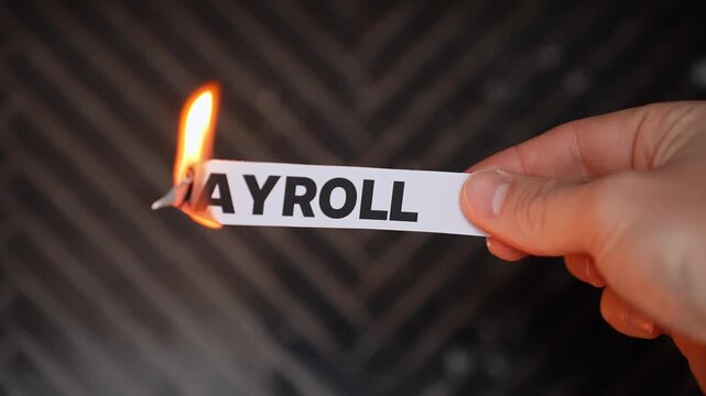 Hand burns a paper label reading &ldquo;PAYROLL,&rdquo; symbolizing payroll costs reduced&mdash;lean operations, higher profit, and automated business systems. Dark background with copy space.