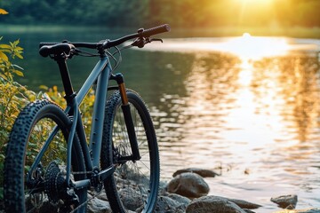 Fototapeta premium mountain bike parked on rocky lakeshore at golden sunset with calm water reflection, peaceful adventurous mood