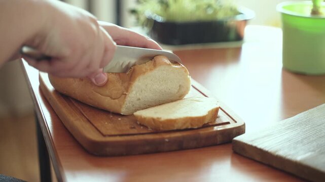Soft and slow cutting of loaf slice on cutting board, closeup. Cutting with knife in sawing motions of fluffy white bread for sandwich cooking at home.