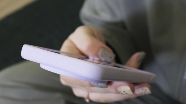 A close-up view of a woman's hand with speckled nail polish scrolling on a purple smartphone. Concept of modern digital communication, everyday mobile lifestyle, and internet addiction.