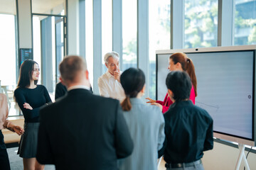 Fototapeta premium Female team leader presents business idea to colleagues standing in modern conference space with digital board. Participants observe visual explanation and exchange opinions. 