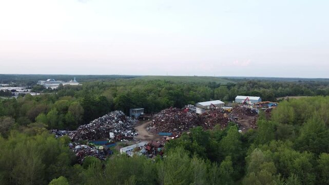 Aerial flight over a scrap metal yard in Cambridge, Ontario, Canada. Piles of scrapper debris in a junkyard among trees.