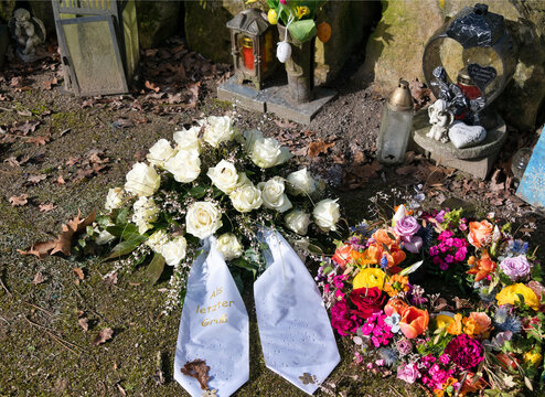 Ein letzter Gru&szlig; mit wei&szlig;en Rosen und einem bunten Kranz auf einem Friedhof in Unna