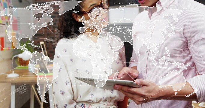 Reviewing tablet, colleagues leaning in at modern office, woman floral blouse, man pink shirt, map