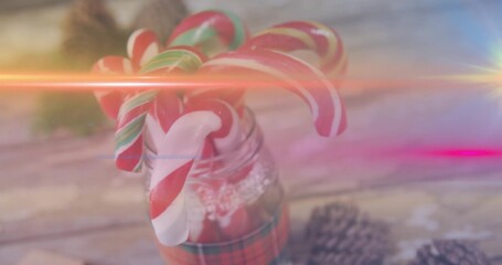 Glass jar wearing lace and plaid ribbon, holding candy canes with pine cones, lens flares