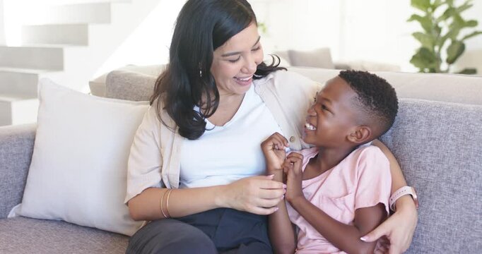 Woman in beige cardigan tickling African American boy on gray sofa bonding playfully smoothing hair