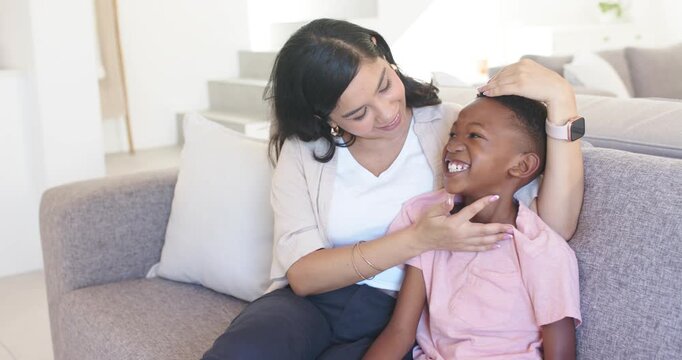Diverse mother cradling son and playfully tickling him on gray couch in living room comforting