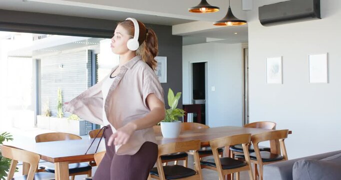 African American woman, white headphones playing music, entering dining room, dancing around table