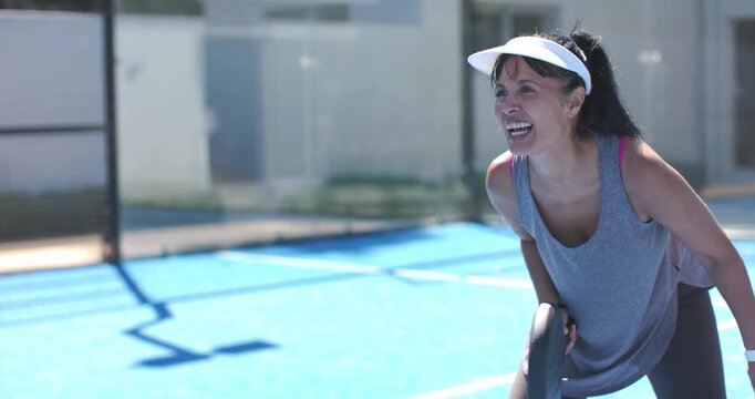 Shifting woman wearing grey tank tracking off-camera ball on blue court, holding paddle, copy space
