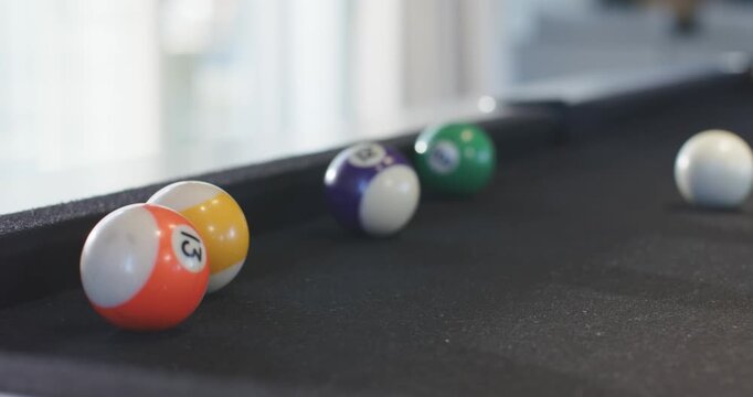 White cue ball rolling across felt pool table after strike, nudging numbered balls along left rail