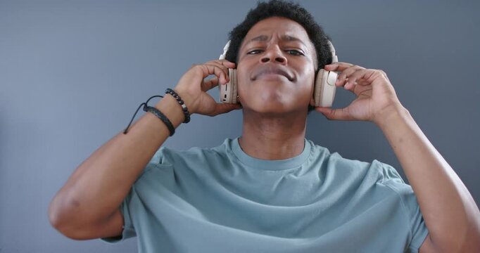 Adult African male testing headphones, adjusting earcups for sound and fit in front of gray wall