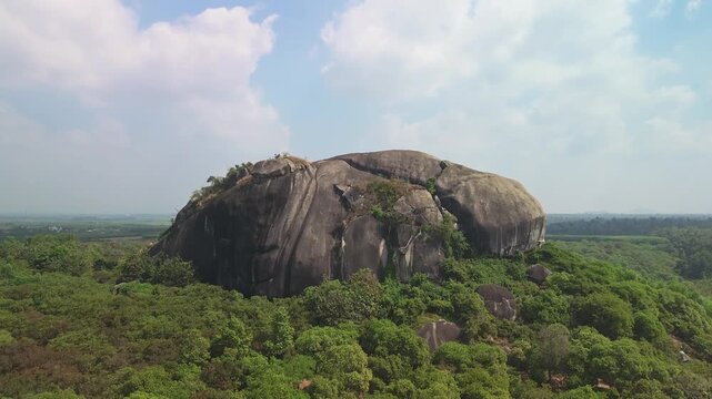 Drone rising to reveal a massive inselberg surrounded by dense forest in Phu Dien, Southern Vietnam