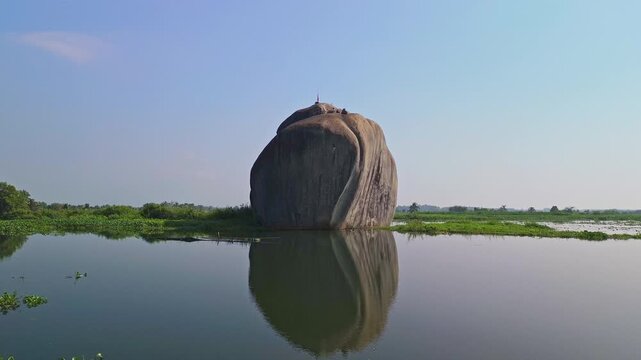 Low drone approach toward an inselberg rising from a calm pond with reflections in Phu Dien, Southern Vietnam