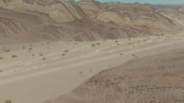 Aerial Drone Shot Revealing Car Driving Through Desert with Wavelike Rocky Mountain Landscape in Namibia