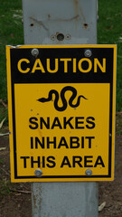 Fototapeta premium Yellow and black caution sign warning snakes inhabit this area mounted on metal post outdoors