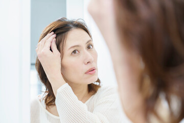 鏡を見て、薄毛を気にするミドルエイジの日本人女性 © gohan