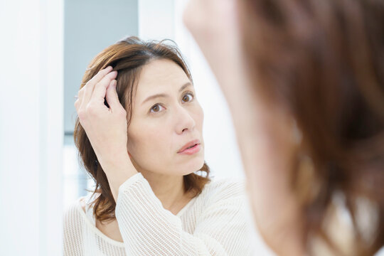鏡を見て、薄毛を気にするミドルエイジの日本人女性